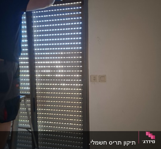 אדם מתקין תריסים בחלון עם סולם
